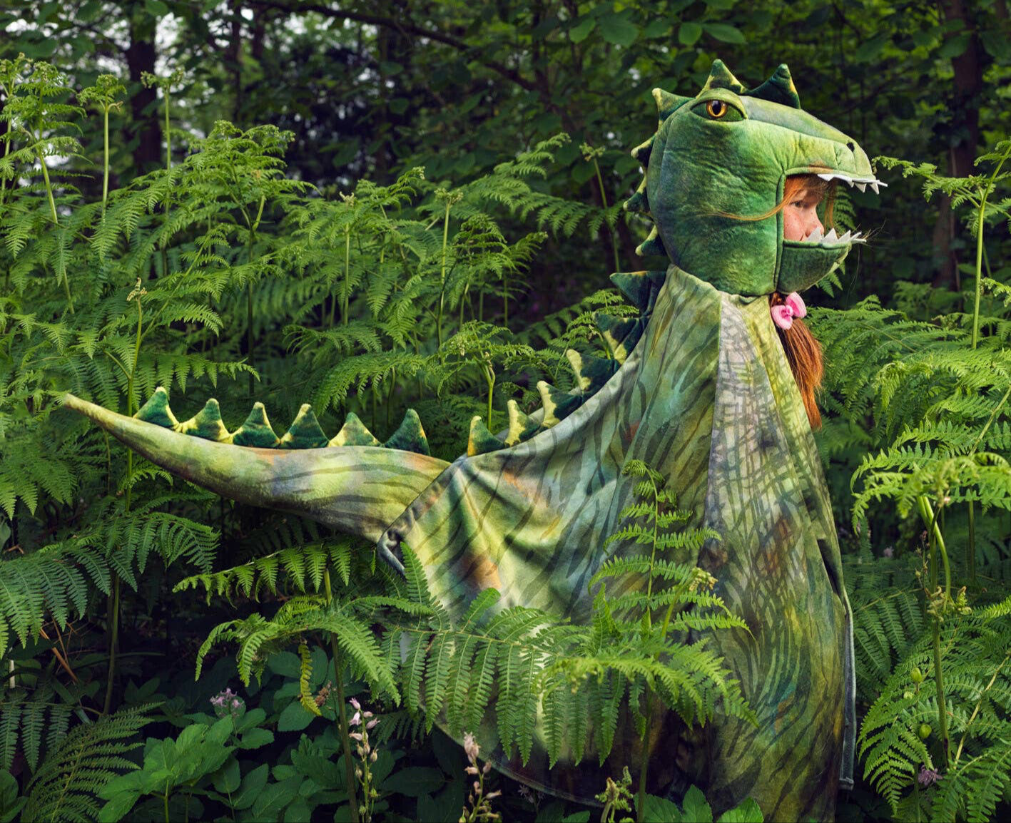 Child in a green dinosaur costume standing in a forest
