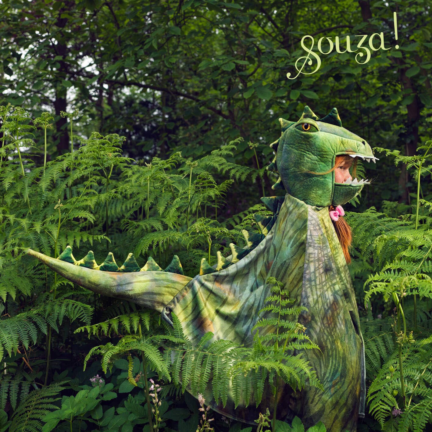 Child in a green dinosaur costume standing in a forest