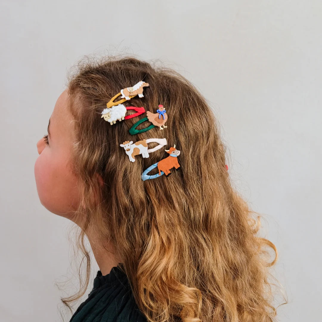 A side-profile view of a child wearing several small animal-shaped hair clips in white, red, green, blue, and orange against a plain light gray background.