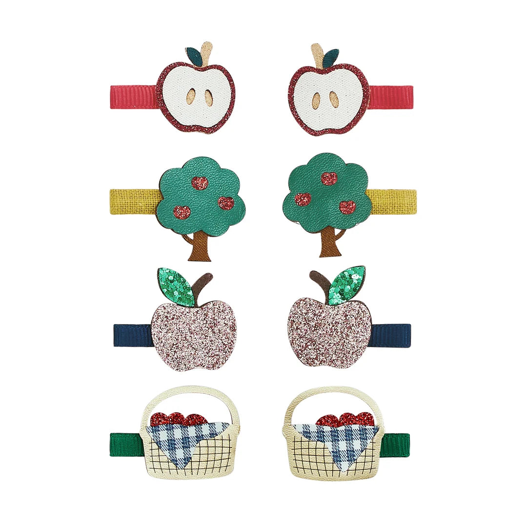 A side-profile view of a young girl with wavy light brown hair wearing a row of colorful decorative hair clips shaped like picnic items and fruit on a plain light gray background.