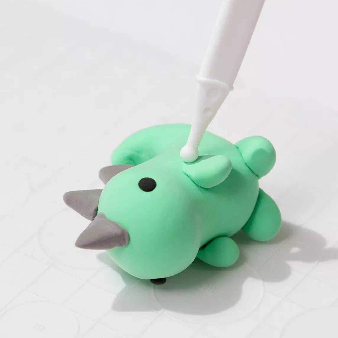 Green dinosaur-shaped phone stand with a white pen on a light gray background