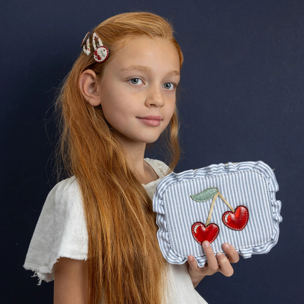 Young girl holding a small handbag with cherry design against a dark background