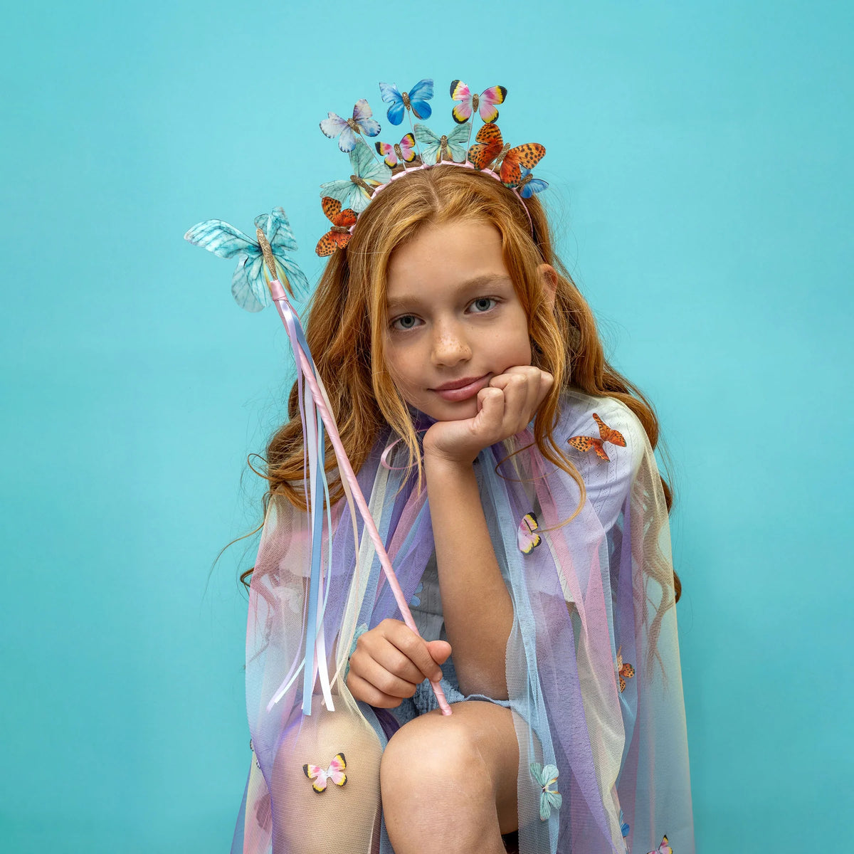 Young girl with butterfly-themed headband,cape and wand against a blue background