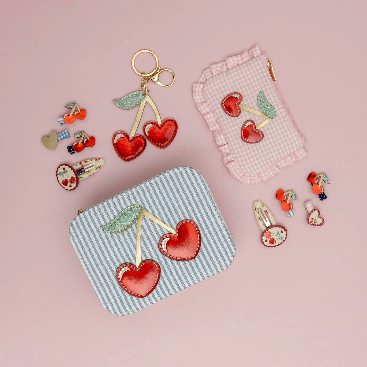 Cherry-themed accessories including keychains and pouches on a pink background