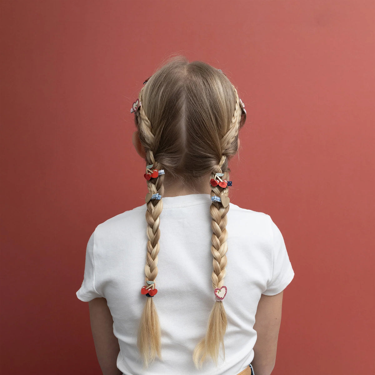 Child with braided hair wearing cherry heart clips against a red background