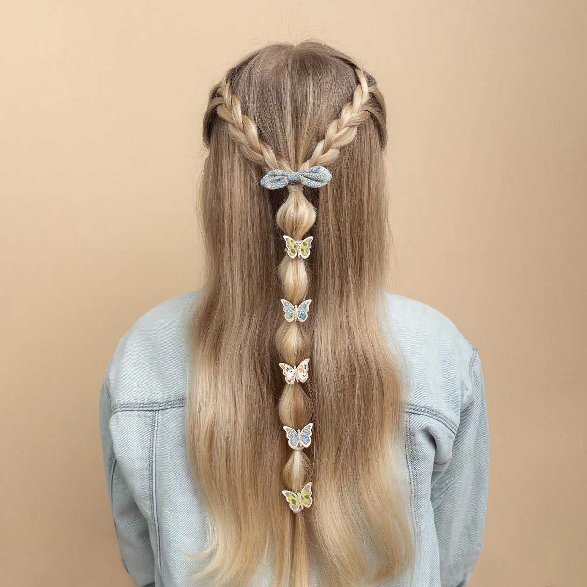 Long blonde hair styled with braids and butterfly hair accessories on a beige background