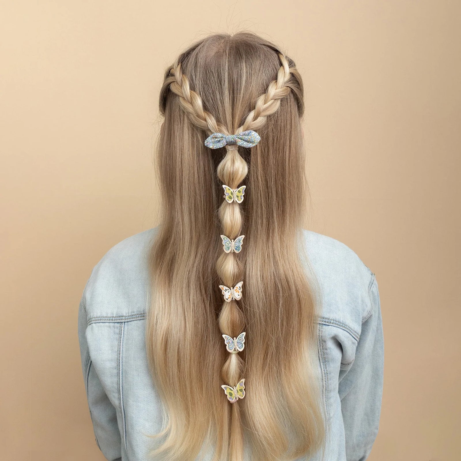 Long blonde hair styled with braids and butterfly hair accessories on a beige background
