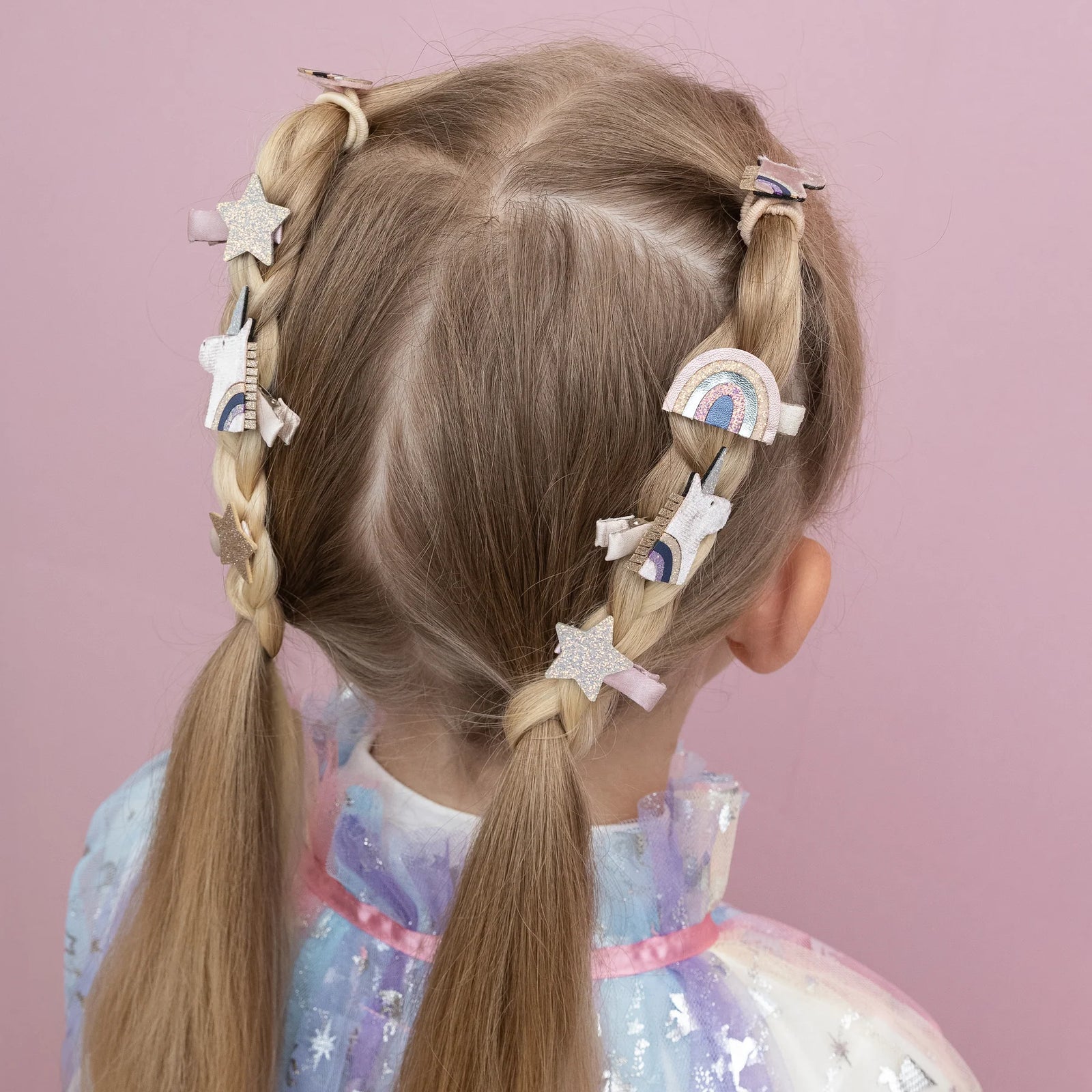 Child with braided hair wearing colorful hair clips on a pink background