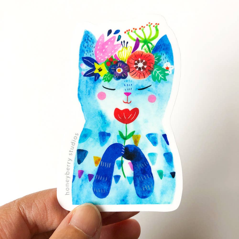 Colorful cat-shaped sticker with floral designs held by a hand on a white background