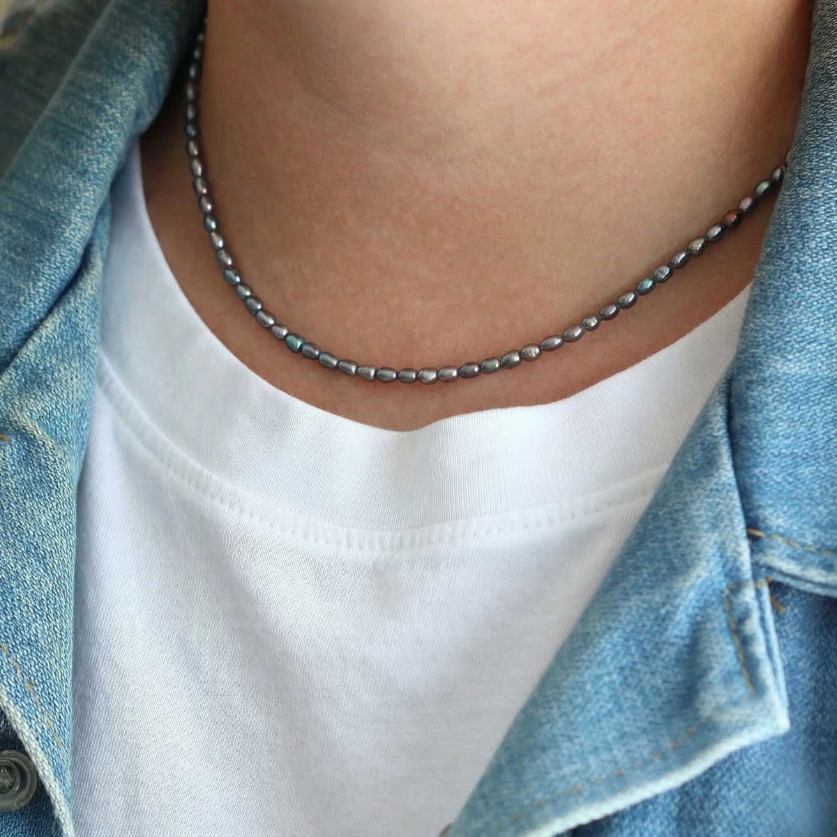 Person wearing a pearl beaded necklace with a denim jacket and white shirt