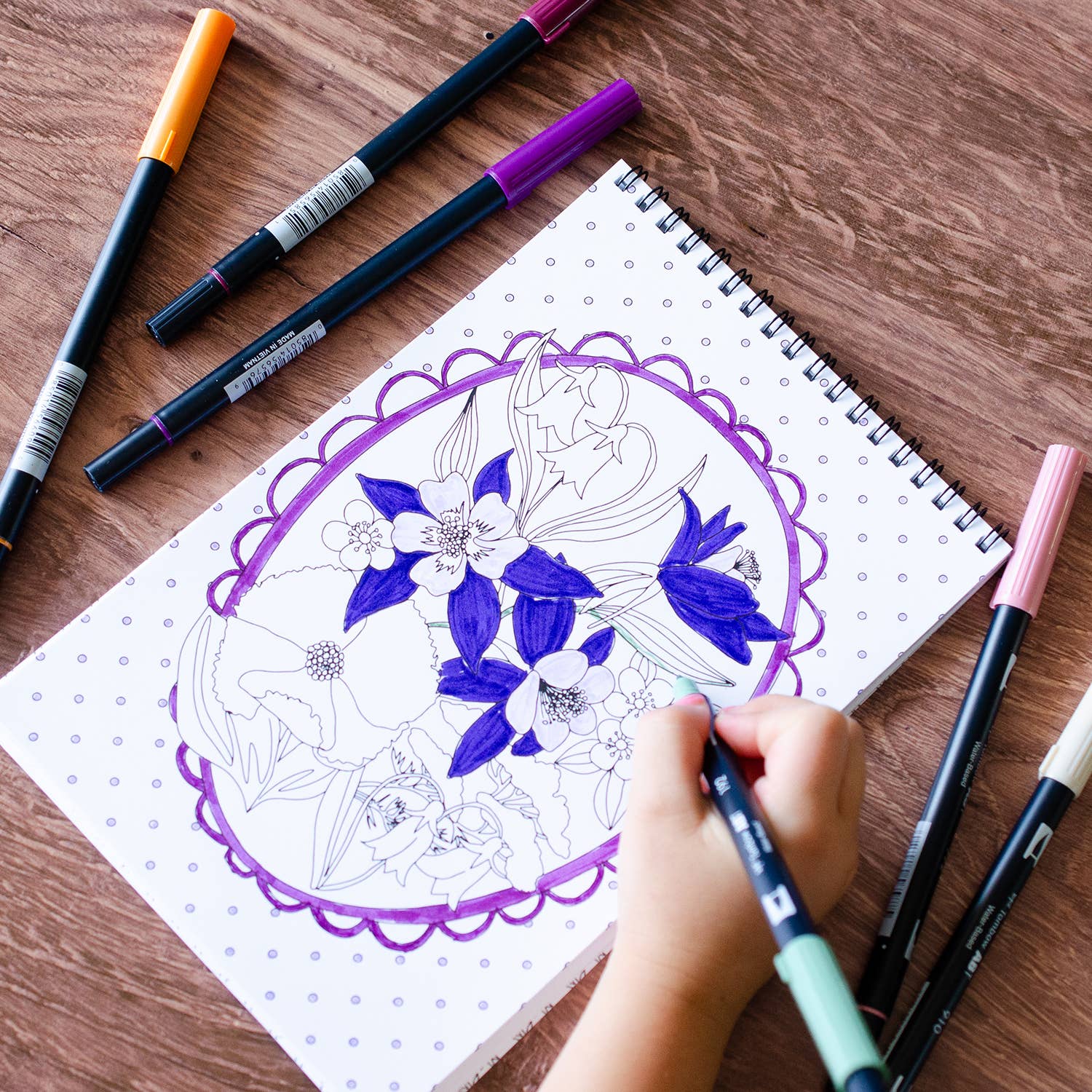Coloring book titled 'Wildflowers' on a wooden surface with markers around it.