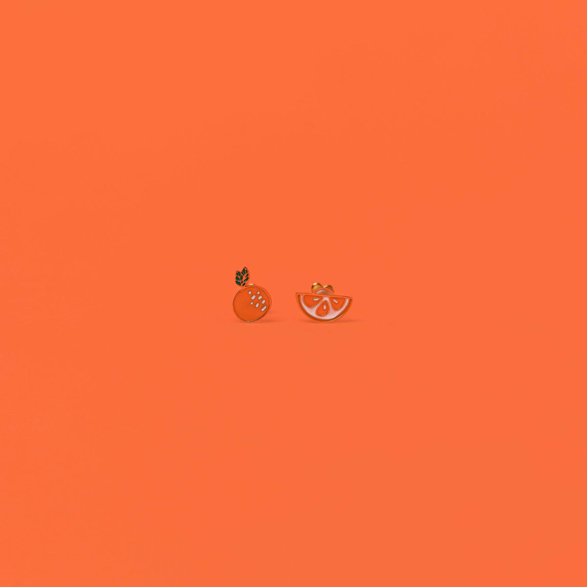 Two small orange earrings on an orange background