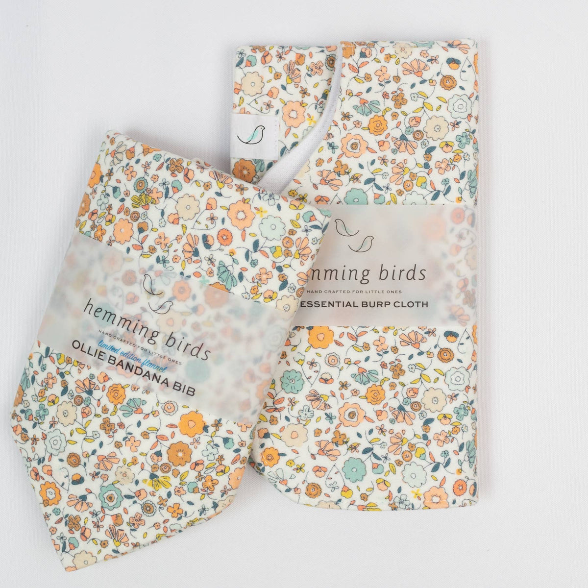 Set of floral-patterned baby bib and burp cloth with &#39;hemming birds&#39; branding on a light background.