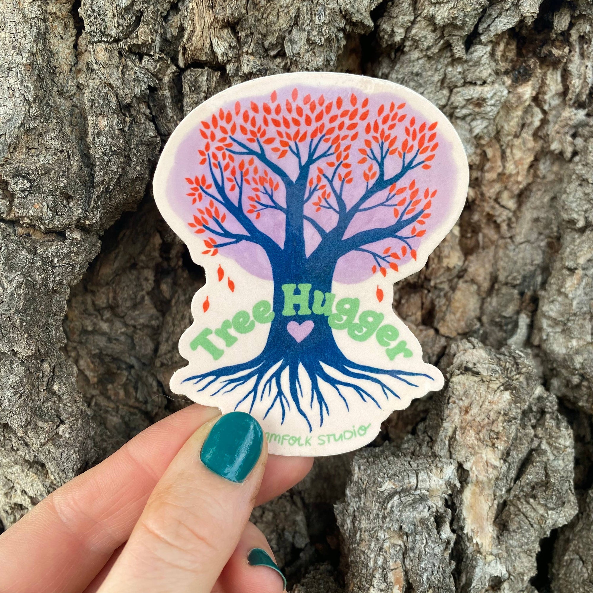 Sticker with tree design and 'Tree Hugger' text held in front of a tree