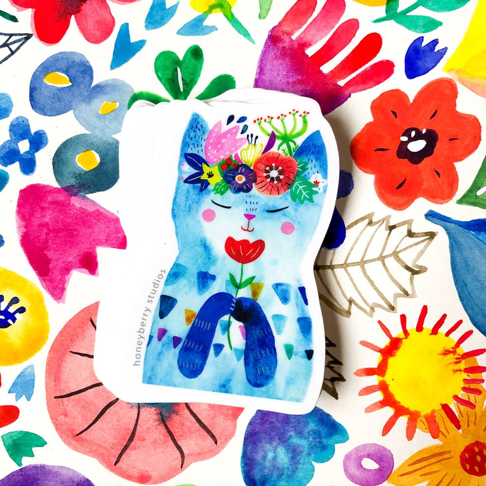 Colorful cat-shaped sticker with floral designs held by a hand on a white background