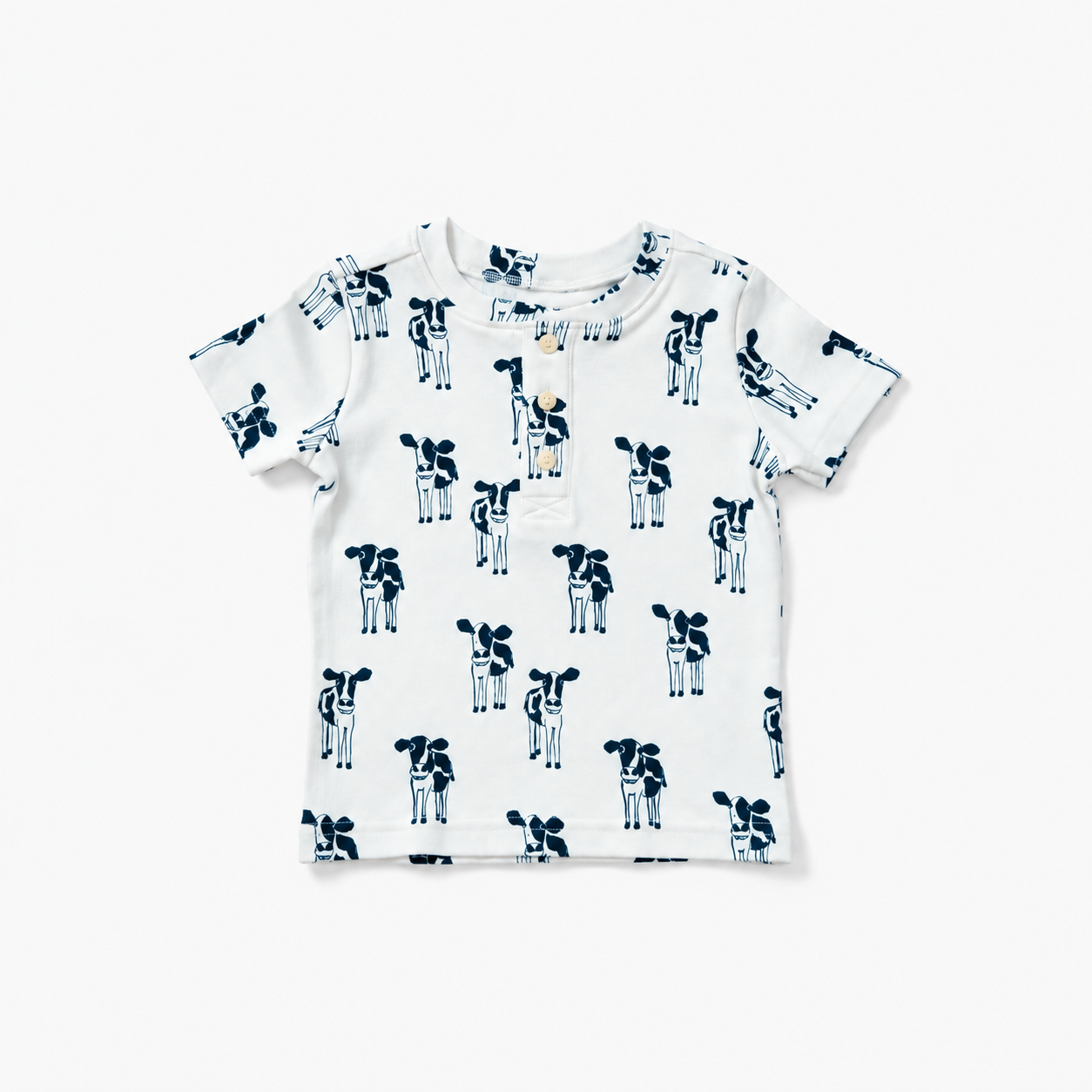 A white short-sleeve baby t-shirt with an all-over navy blue cow print, laid flat against a clean white background.