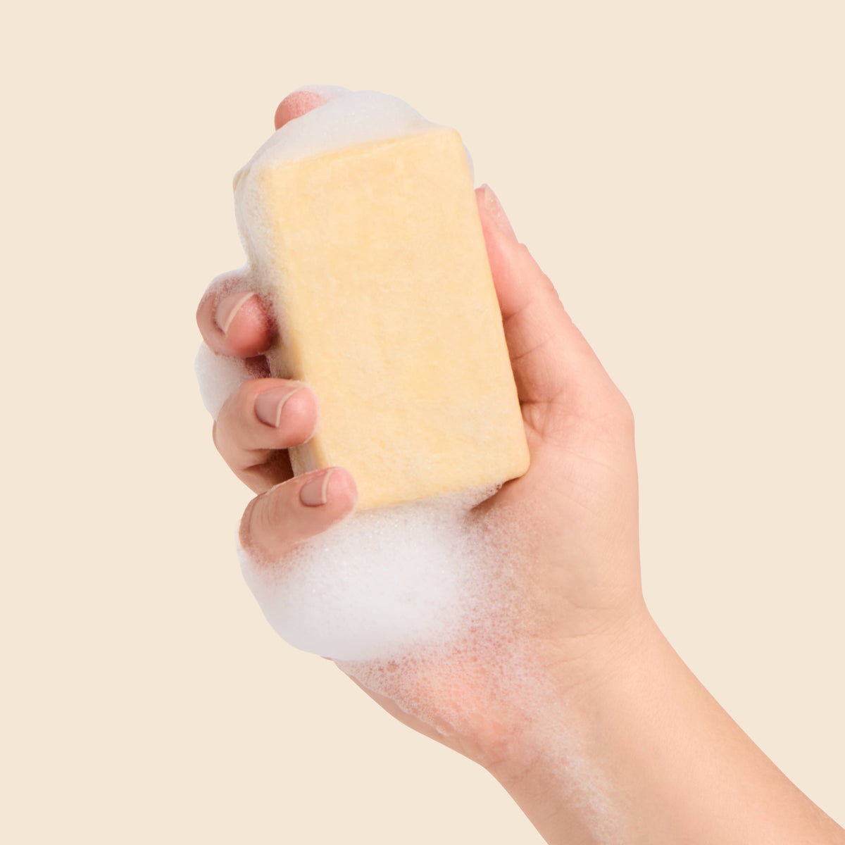 Hand holding a yellow sponge with foam against a beige background
