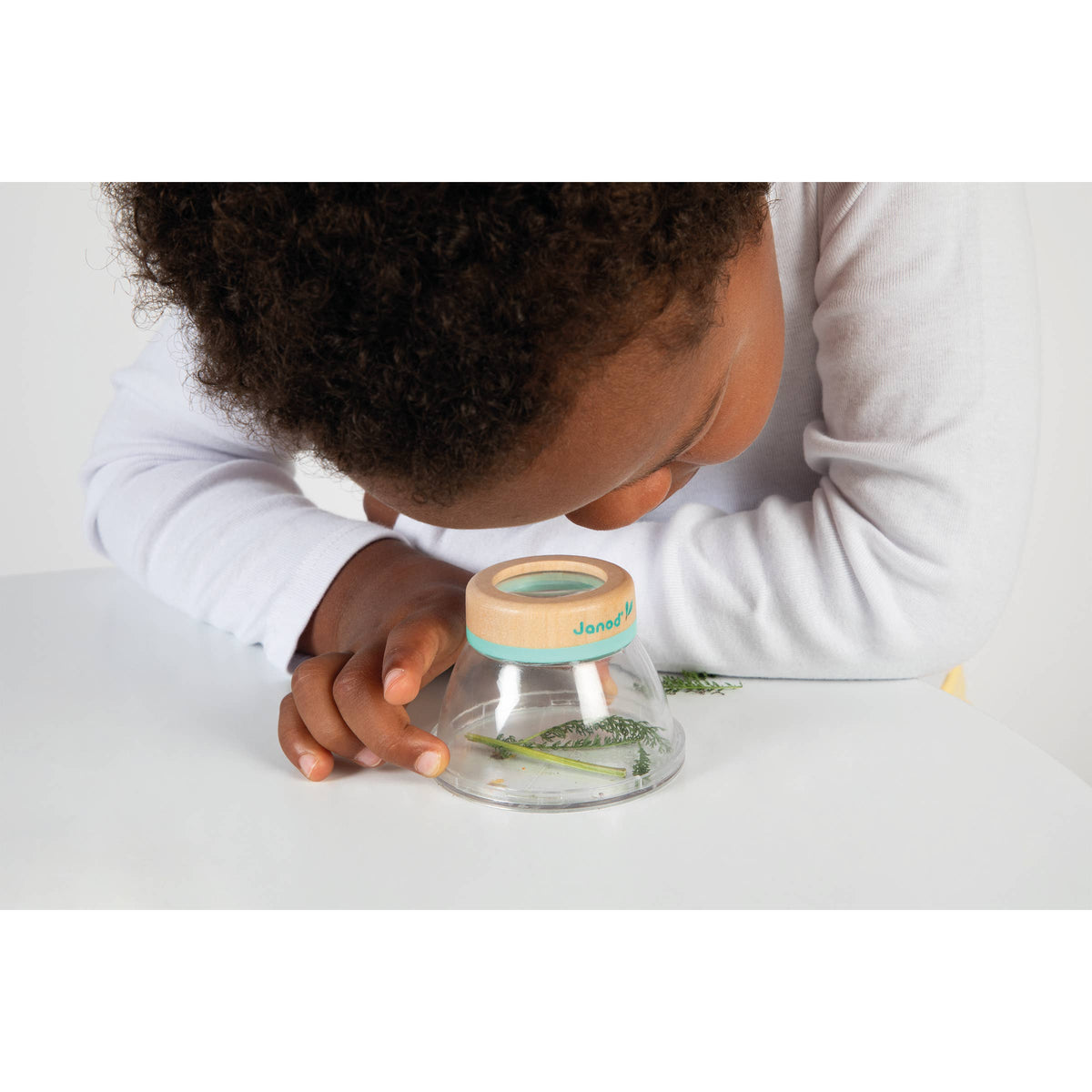 Child looking into a clear container with a wooden lid on a white surface