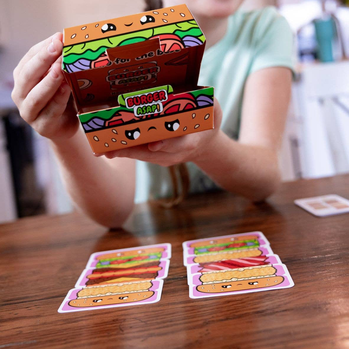 Child holding a colorful card with cartoon food designs on a wooden table.