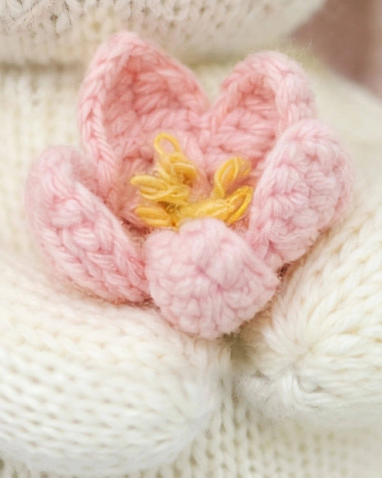 Knitted bunny toy holding a pink flower on a white background