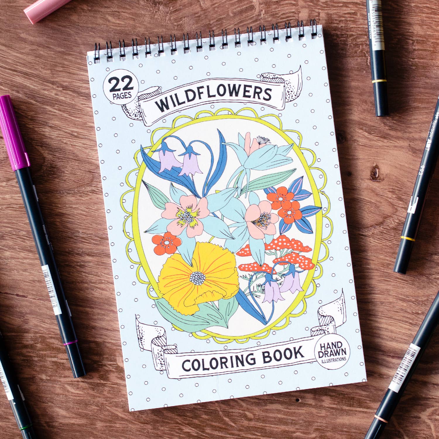Coloring book titled 'Wildflowers' on a wooden surface with markers around it.