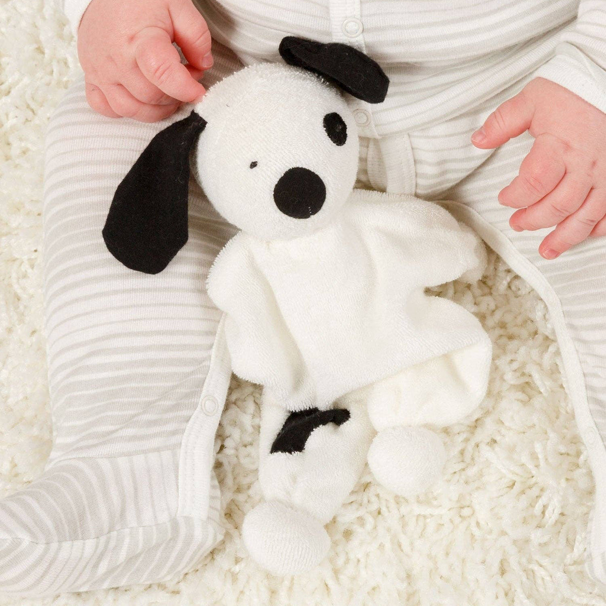 White plush dog toy with black accents held by a child in a white outfit on a white surface