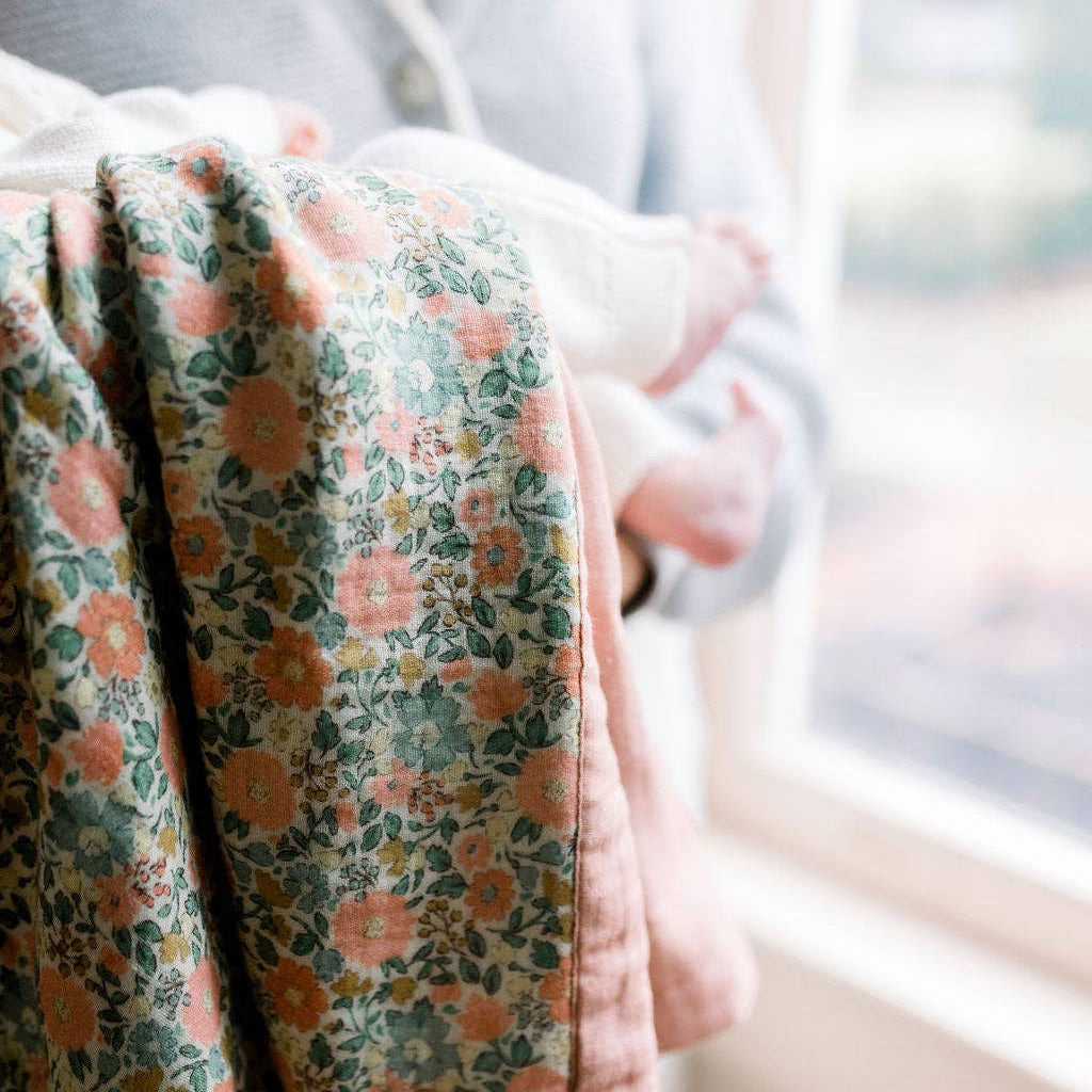 Woman holding a baby wrapped in a floral blanket by a window