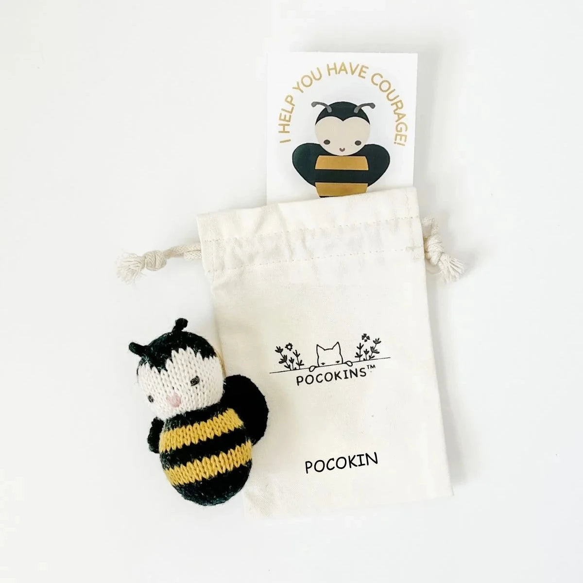 A small knitted bumblebee  toy in black and yellow is displayed next to a cream cotton drawstring pouch and a printed card on a clean white background. The pouch and card are branded with 'POCKOKINS'.