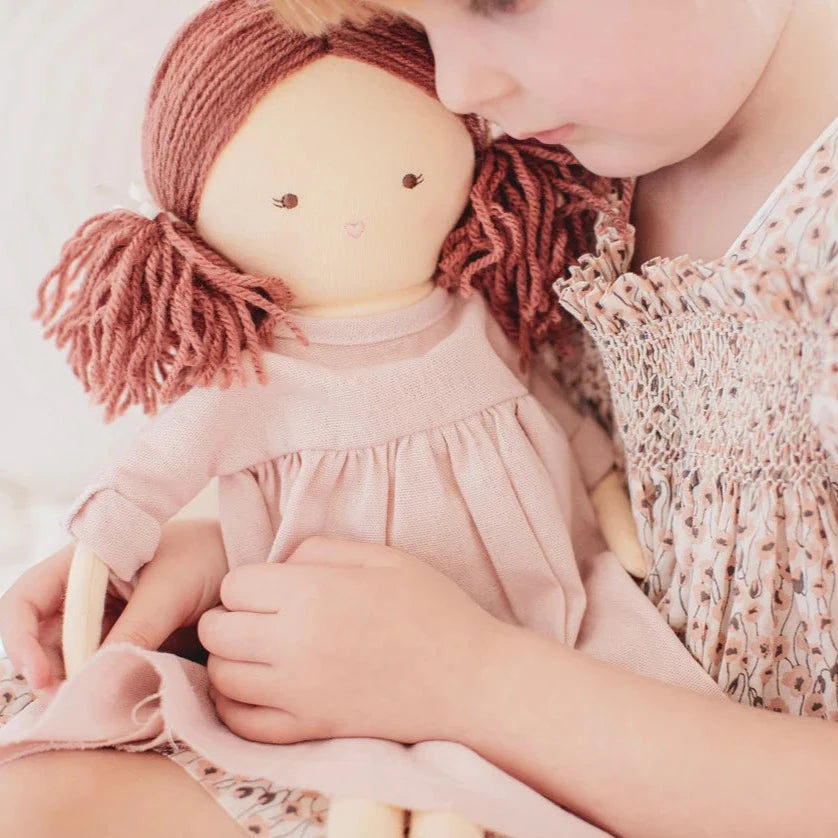 child holding doll with long red ponytails and pink dress