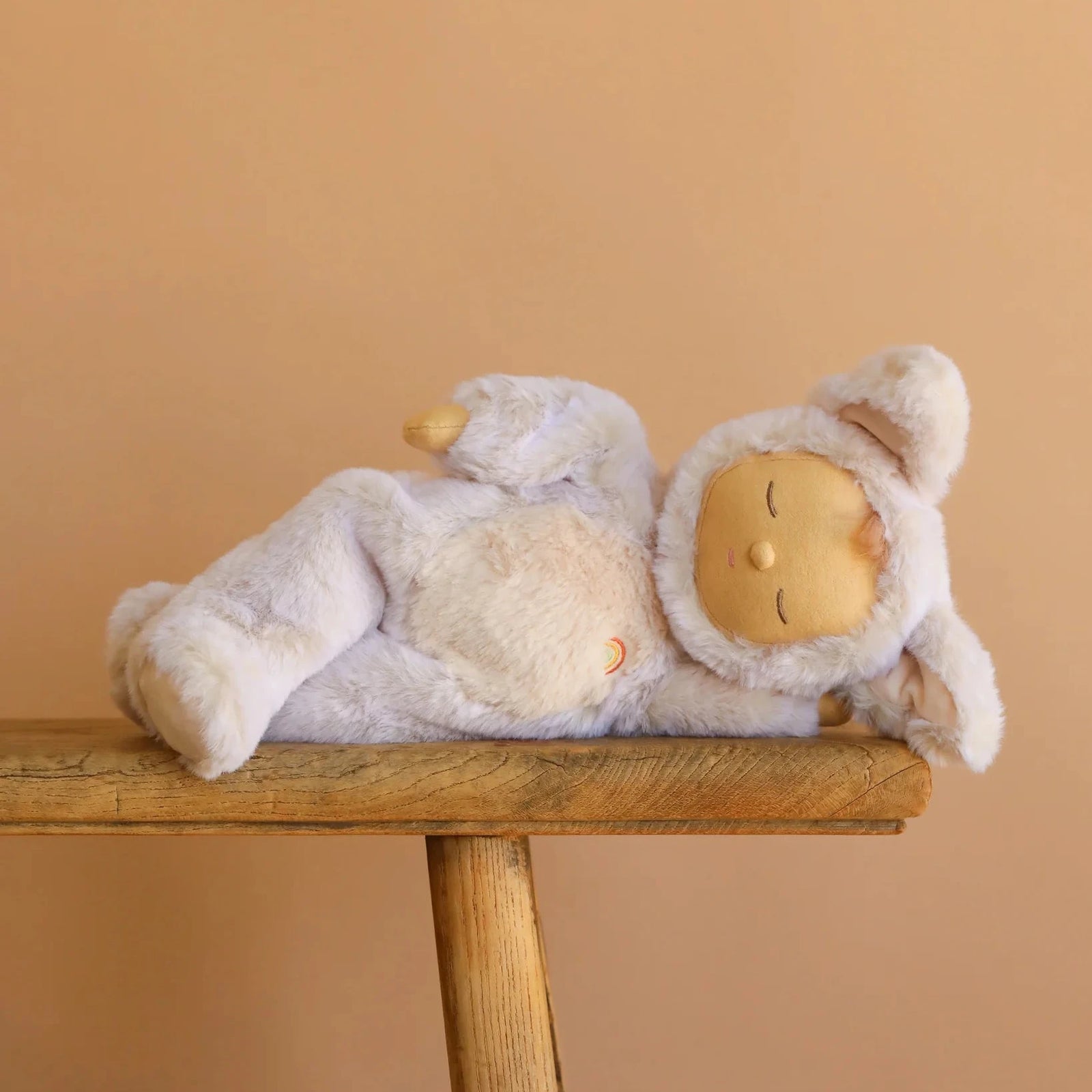 Sleeping fox doll in a white outfit on a wooden stand against a beige background