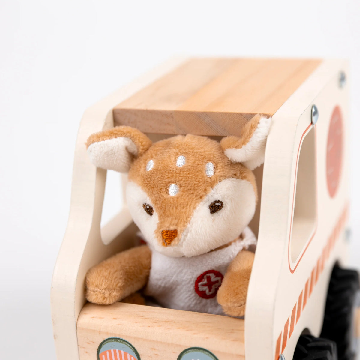 A plush toy deer sitting inside a wooden toy ambulance on a clean white background.
