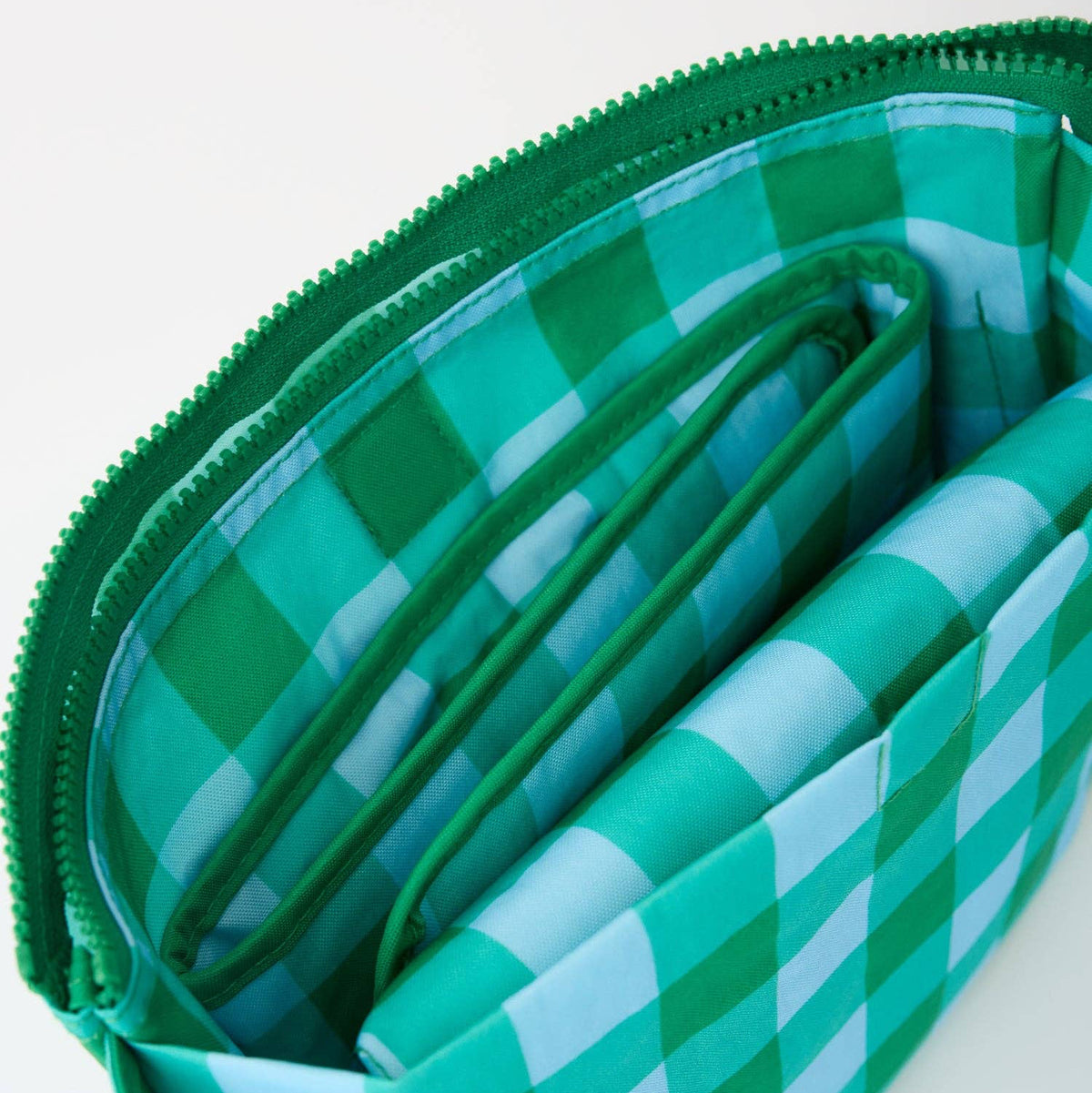 A close-up of a green and white gingham zippered pouch with multiple internal compartments and a matching green zipper.