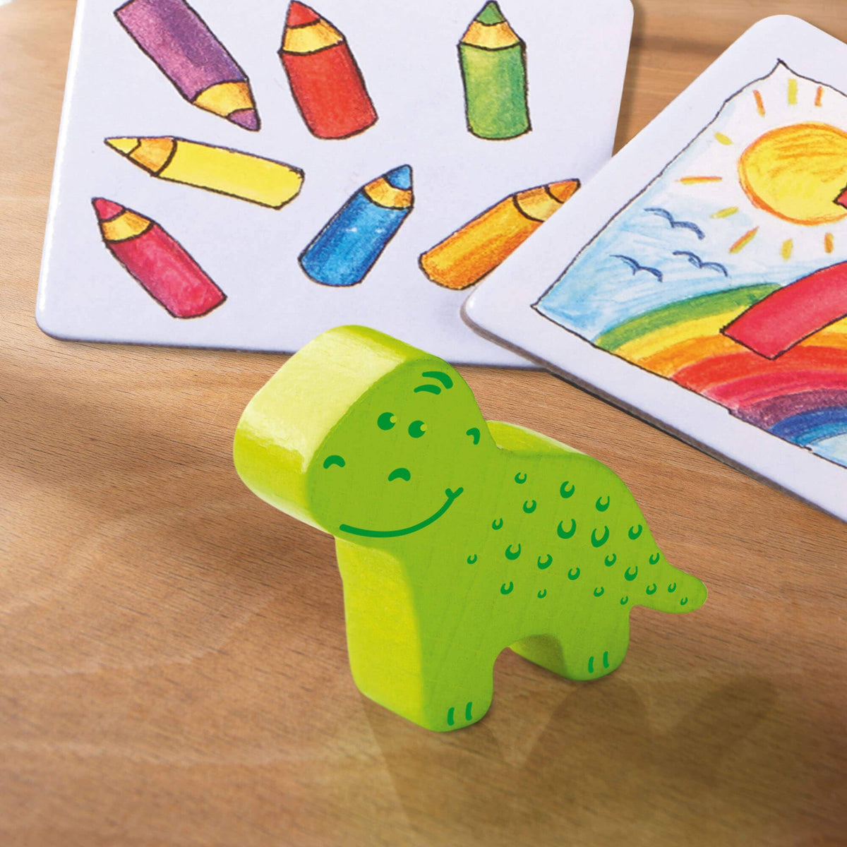 Green dinosaur toy on a wooden surface with game drawings in the background