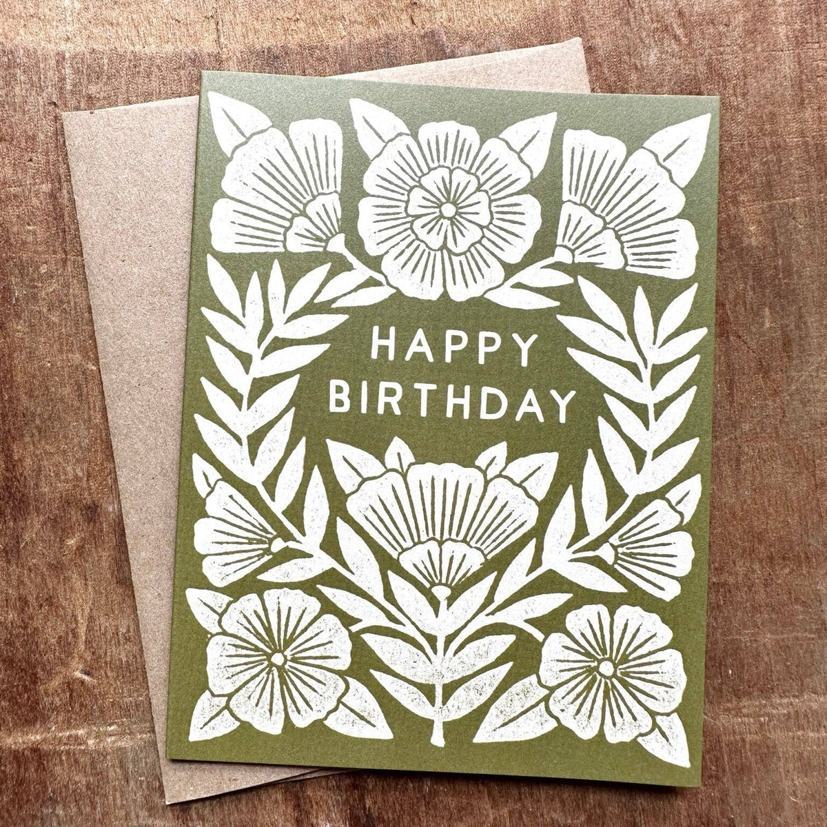 Green birthday card with white floral design and 'Happy Birthday' text on a wooden surface