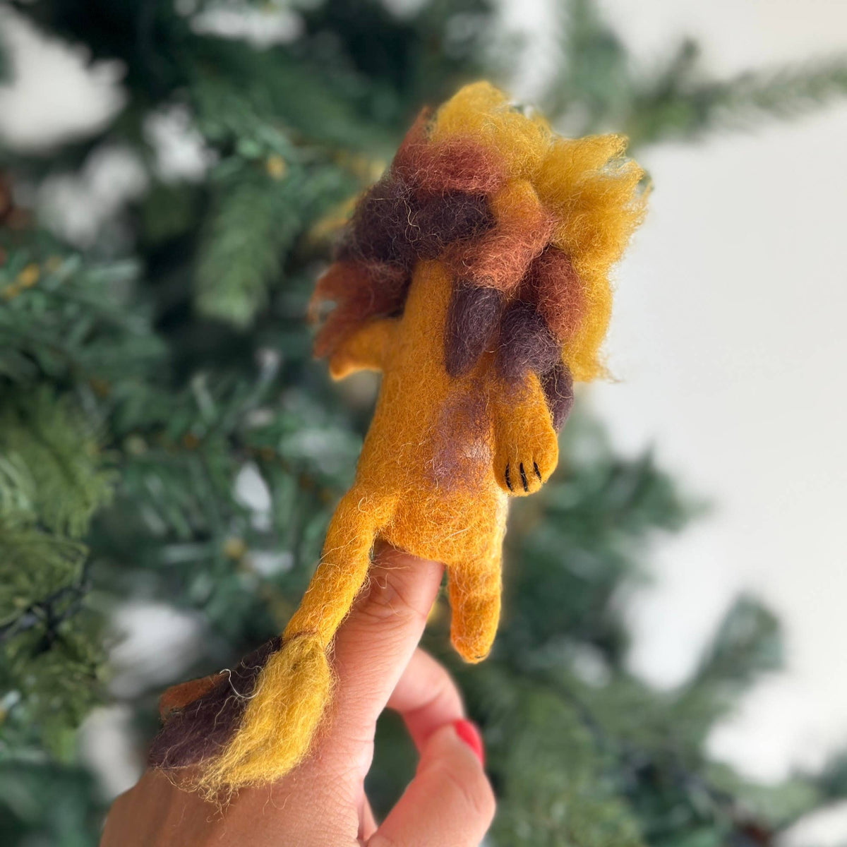 Hand holding a small lion-shaped felted toy against a blurred green background