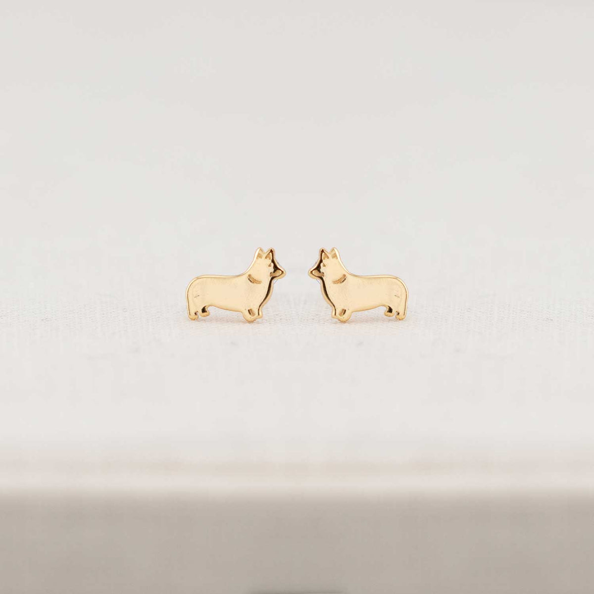 Gold dog-shaped earrings on a light gray background