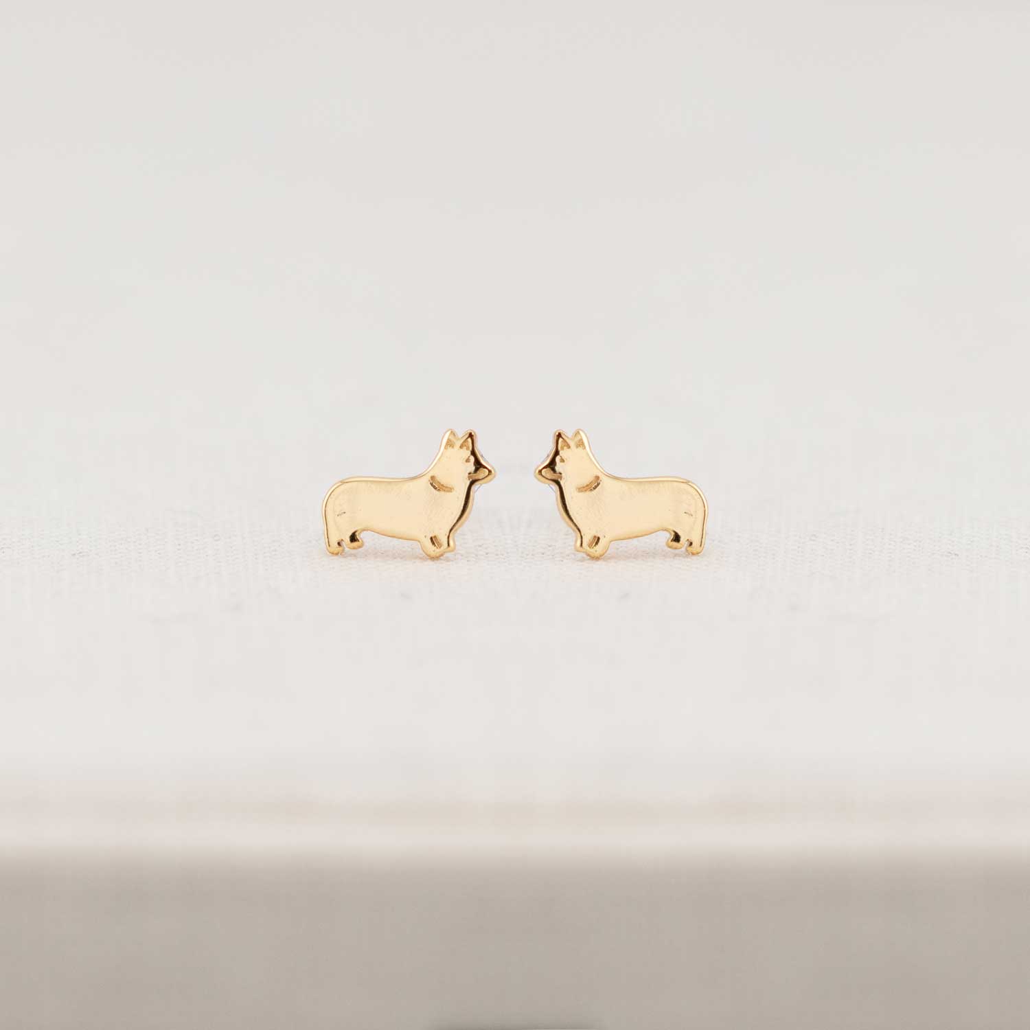 Gold dog-shaped earrings on a light gray background