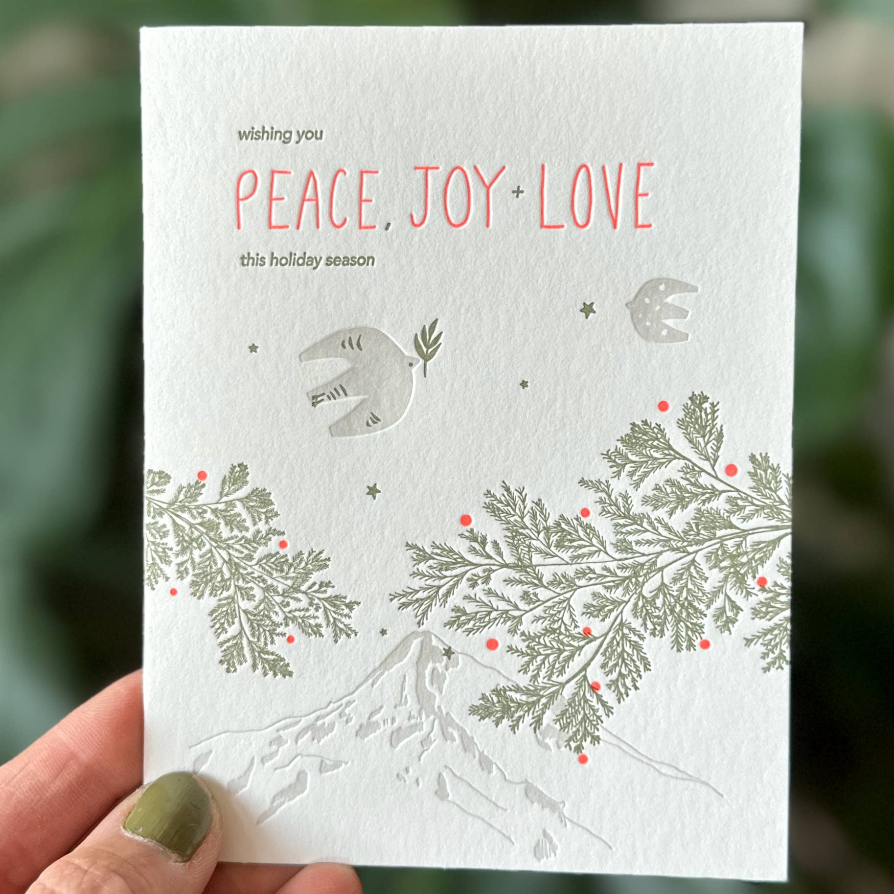 Holiday card with 'Peace, Joy, Love' text and festive designs held by a hand.