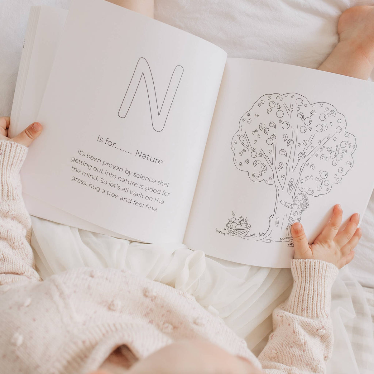 child holding a coloring book open to a page with a tree illustration and text.