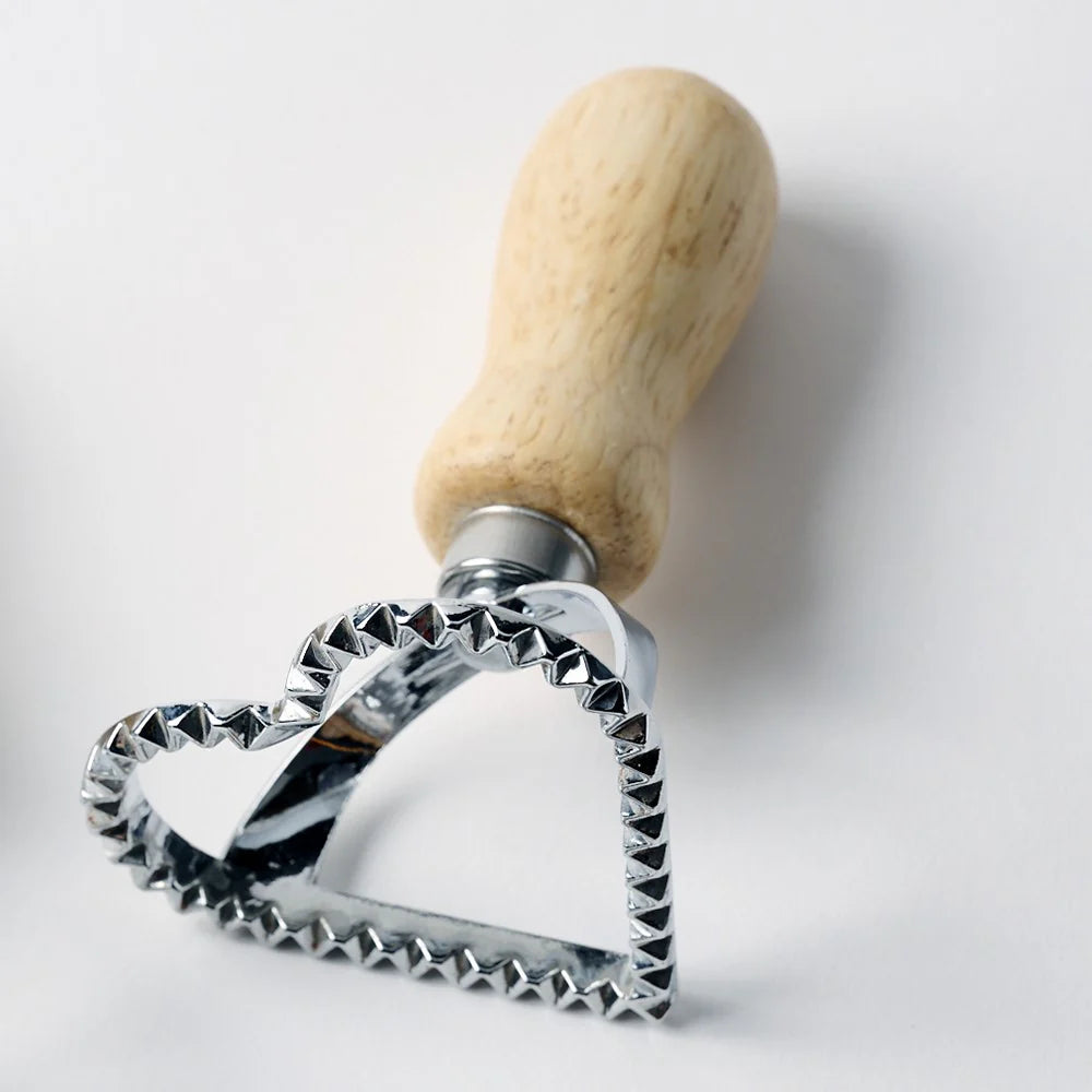 Heart shaped metal cookie cutter with a wooden handle on a white background