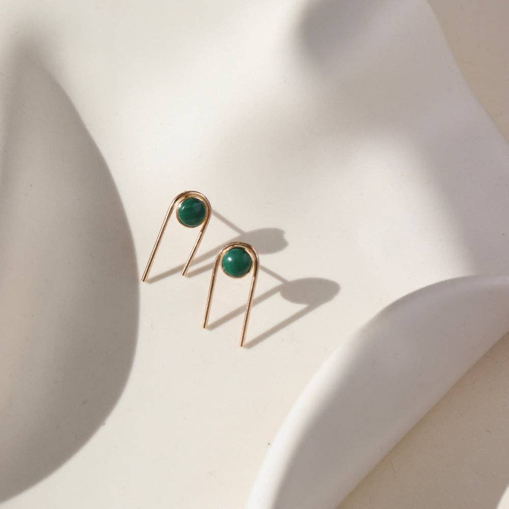 Gold earrings with green gemstones on a light background