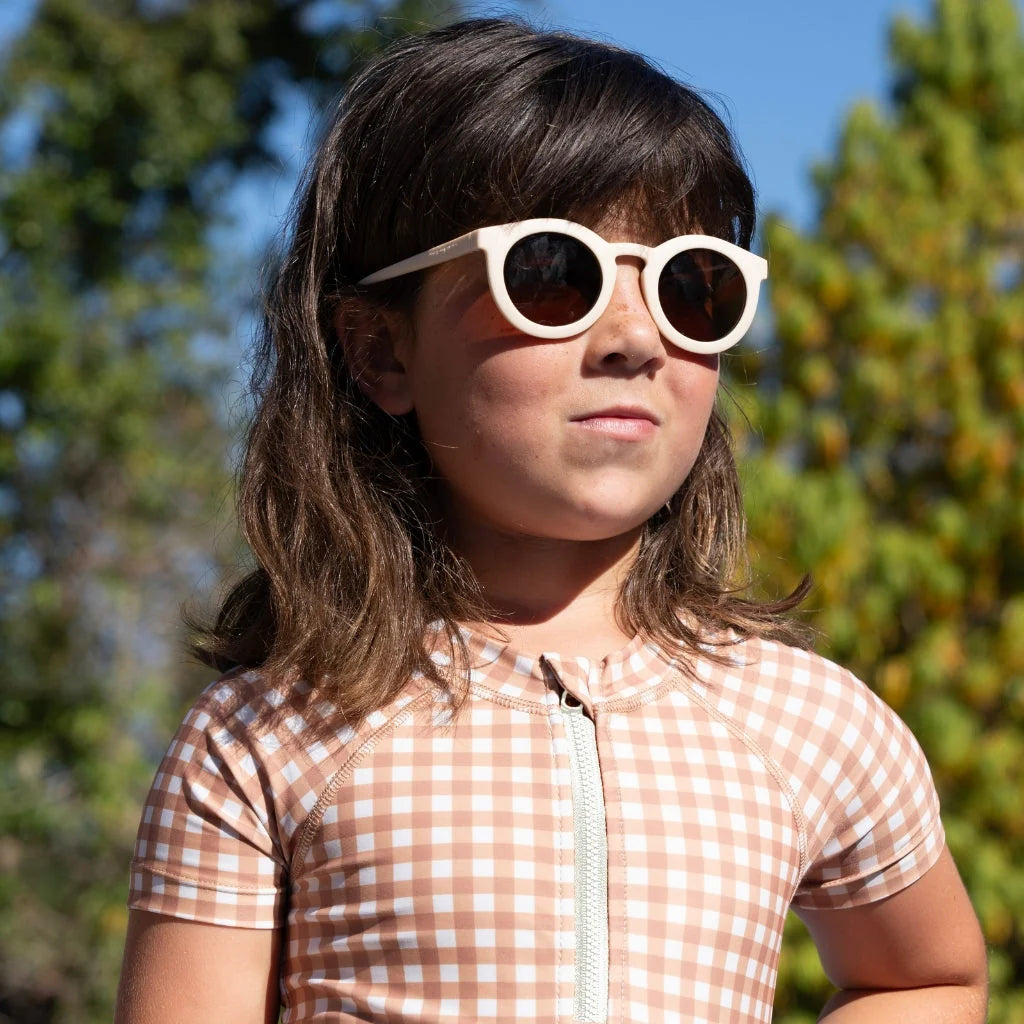 Child wearing white sunglasses with a checkered bathing suit outdoors