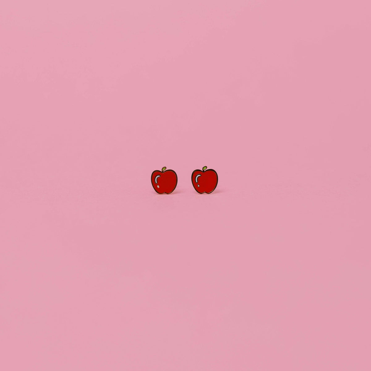 Red apple-shaped earrings on a pink background