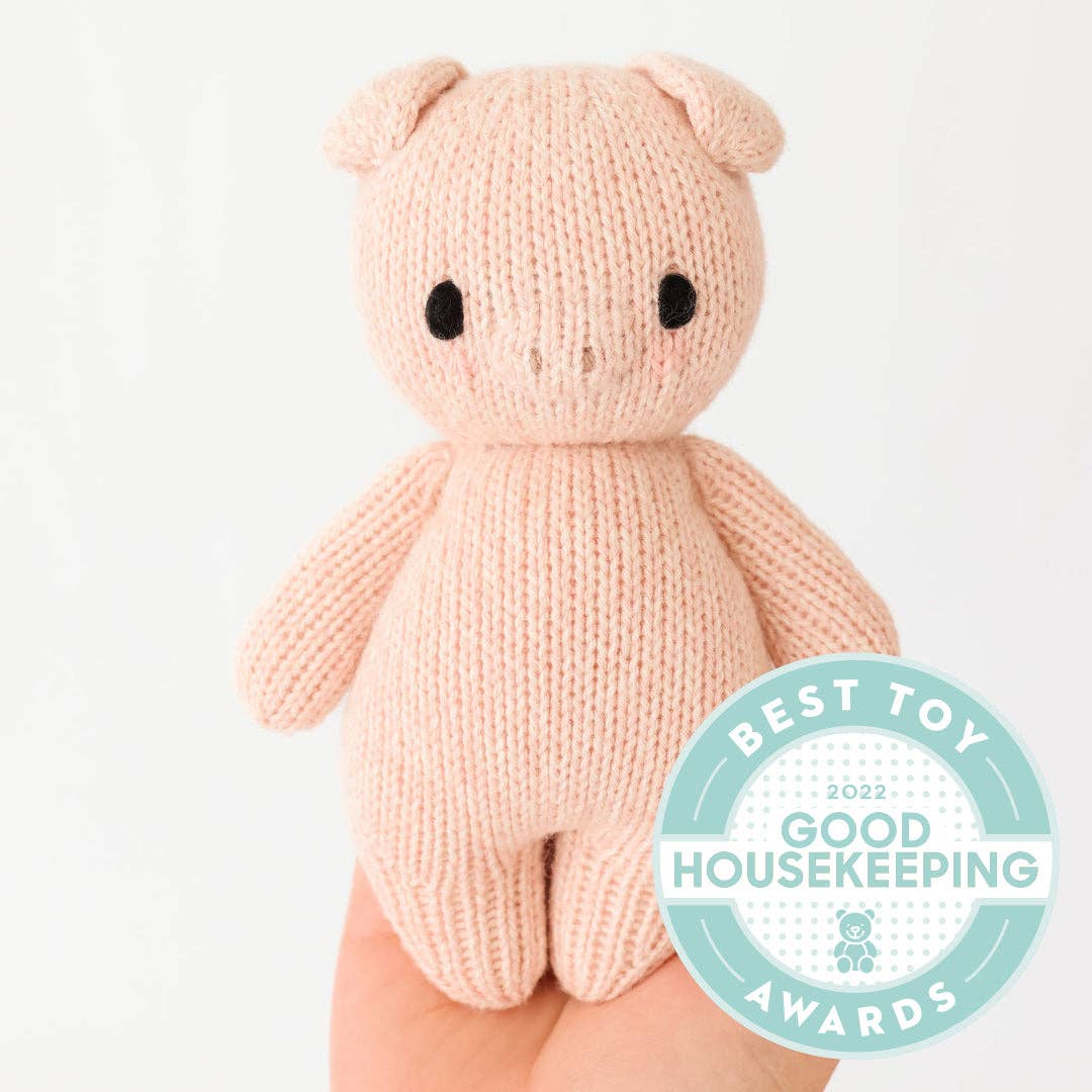 Knitted pink pig toy with Good Housekeeping Award badge on a white background