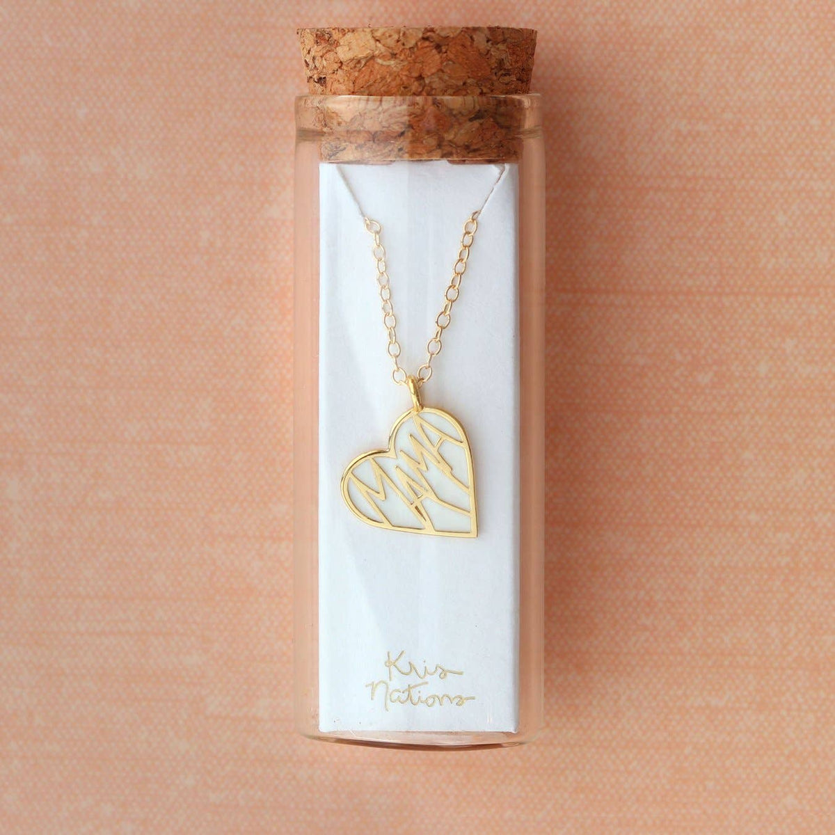 Gold necklace with a heart-shaped pendant in a clear packaging tube on a pink background