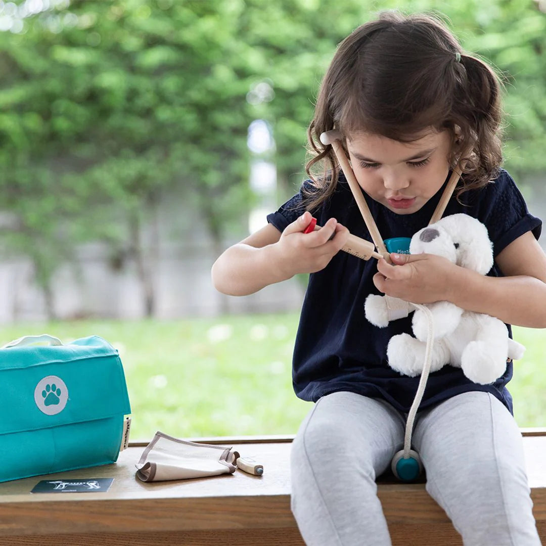 Child playing with a toy dog and a teal bag with a paw print on a wooden surface outdoors.