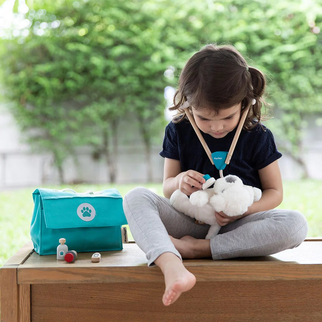 Child playing with a plush toy outdoors, with a teal bag and items on a table in front.