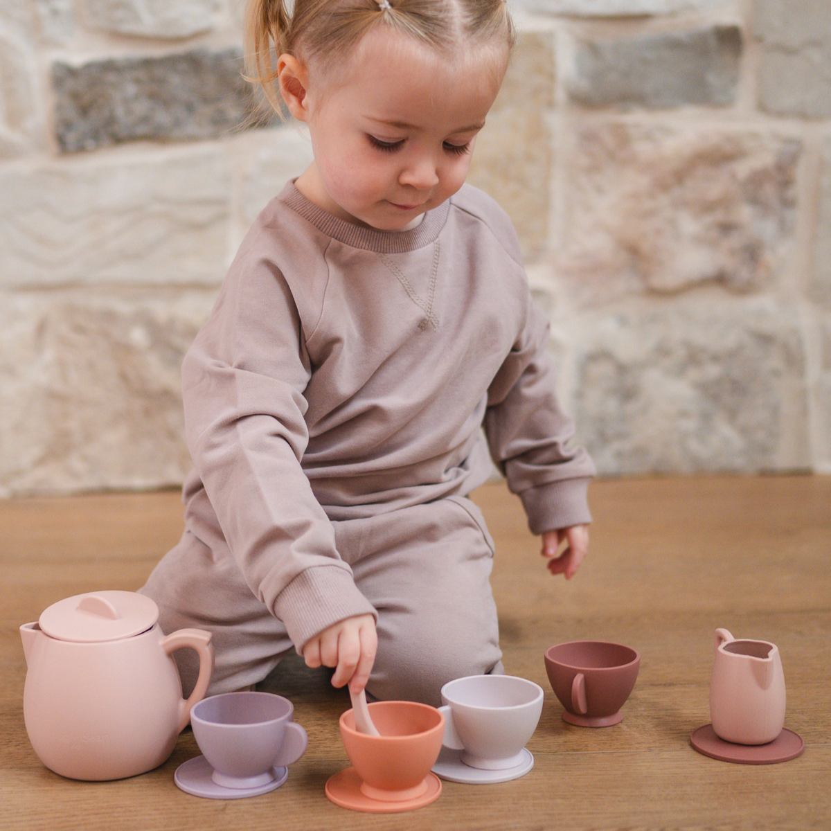 Child playing with a set of colorful silicone tea set on a wooden table.