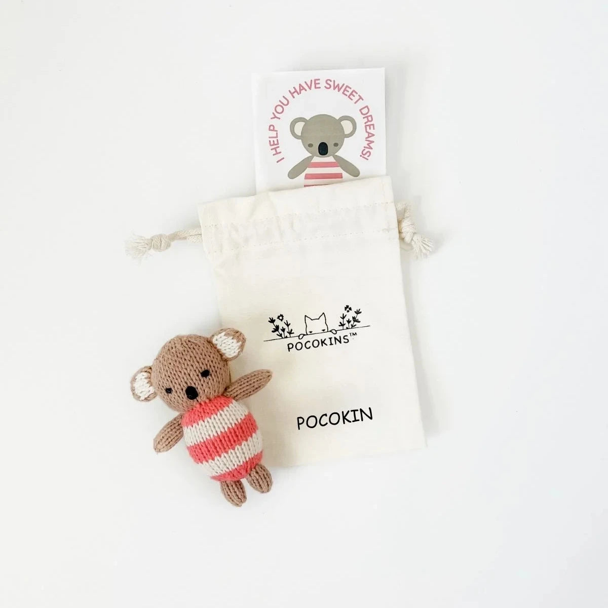 A small knitted koala toy wearing a red and white striped sweater, placed next to a cream drawstring pouch printed with the brand name 'Pocokin' and a small greeting card on a white background.