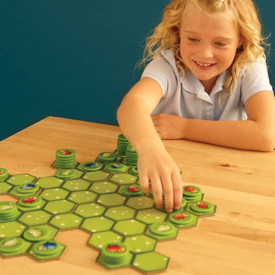 Young girl playing with a green hexagonal board game on a wooden table.